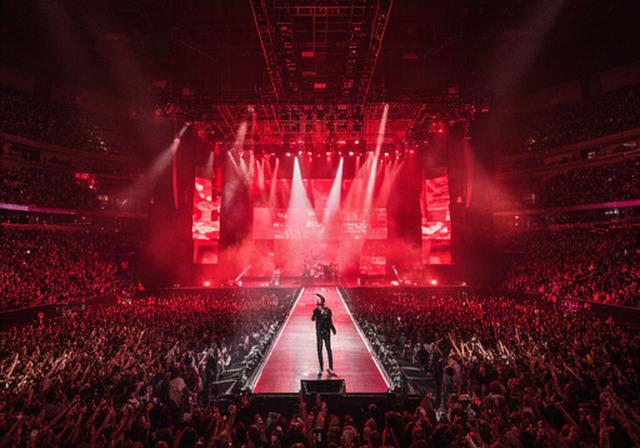 The Weeknd performing live on a massive concert stage with dramatic red lighting and a full arena crowd